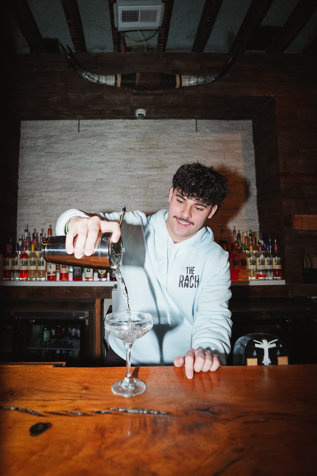 Bartender pouring a cocktail into a glass on the wood bar top