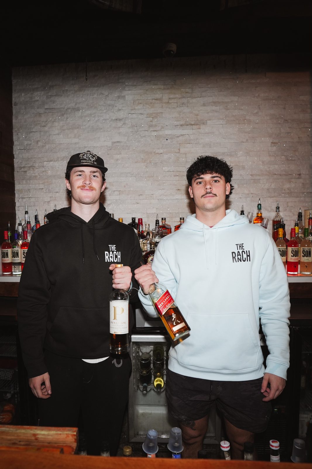 Two bartenders holding whiskey bottles behind the bar